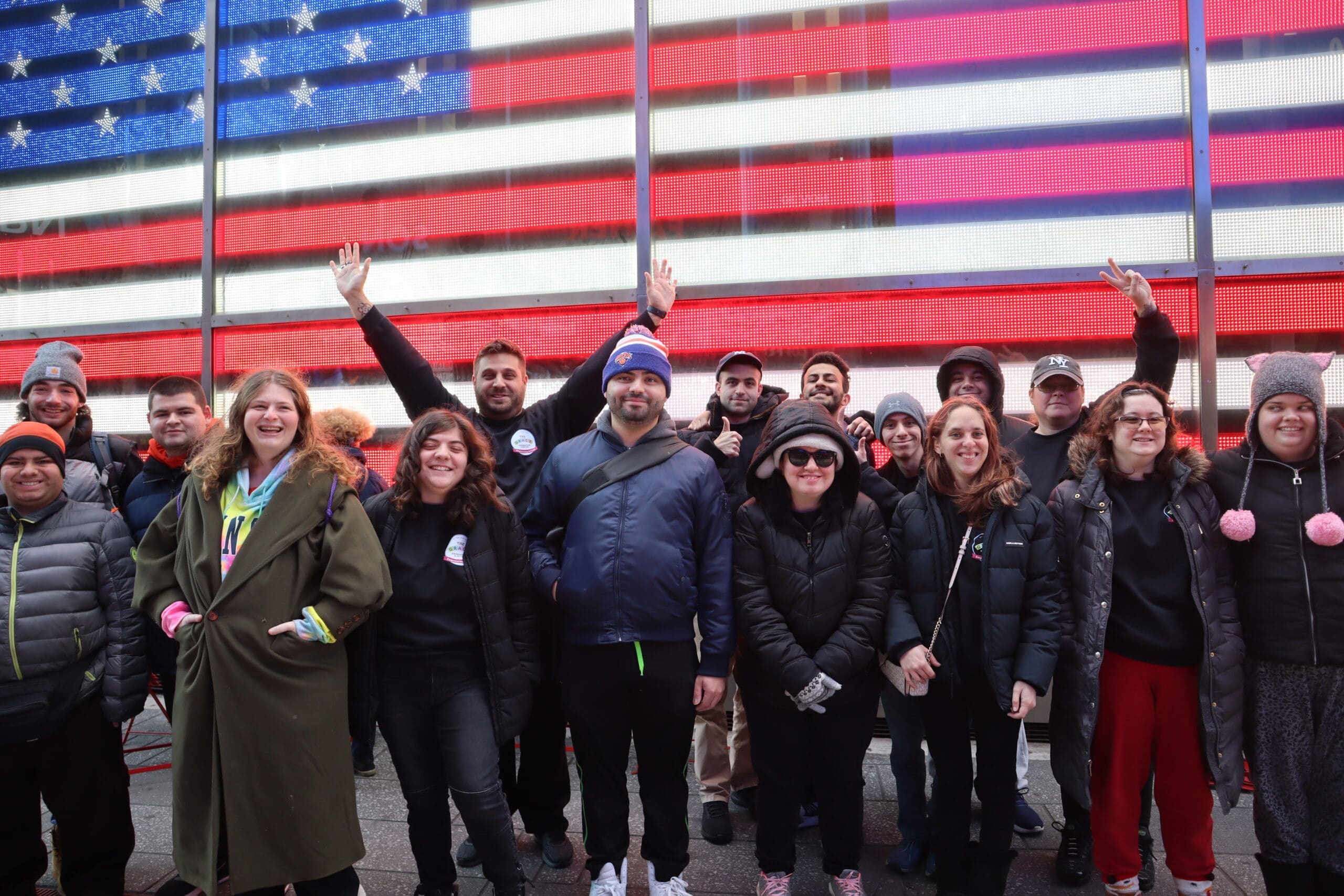 Group of people from The GRACE Foundation smiling and waving in front of an American flag backdrop.